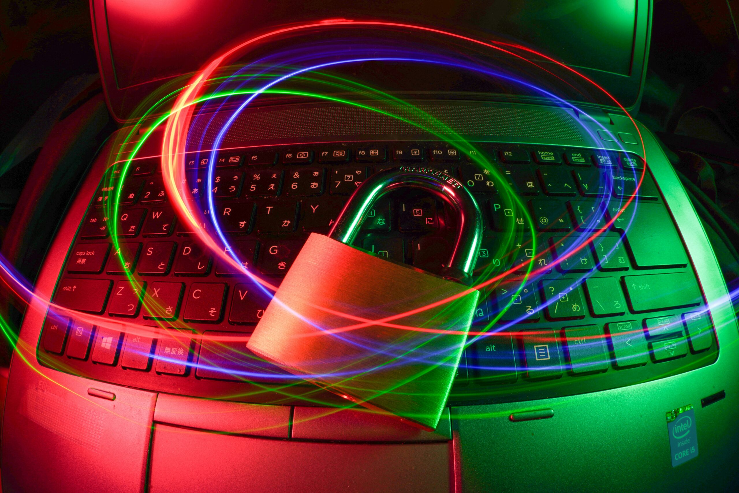 A laptop keyboard with a large padlock in the center, illuminated by red, green, and blue light trails.